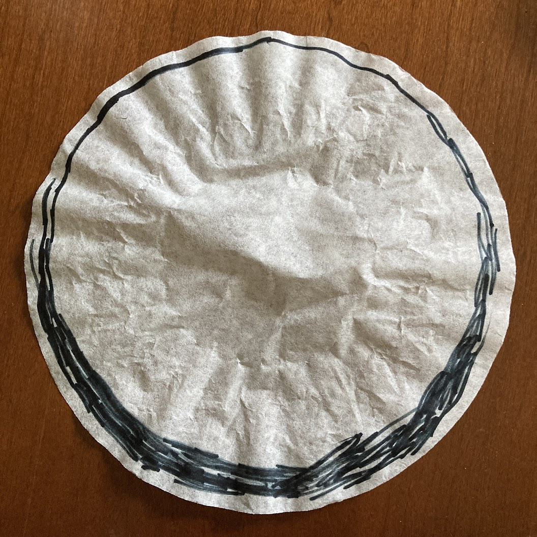 A coffee filter with a sketchy black circle drawn around the outside that is thicker on the bottom than the top.