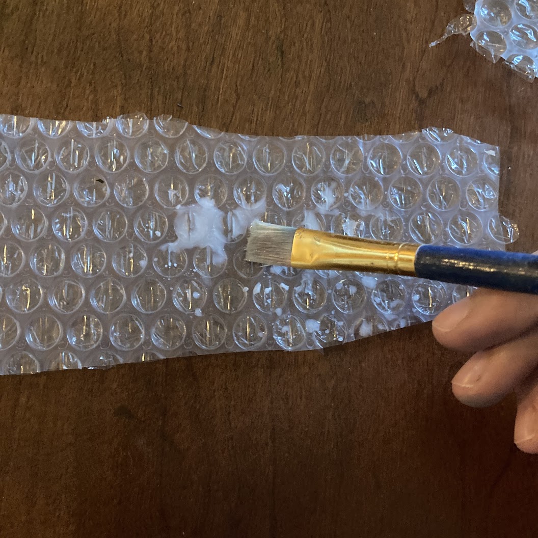 Up close photo of bubble wrap with glue-water mixture being brushed onto it with a paintbrush.